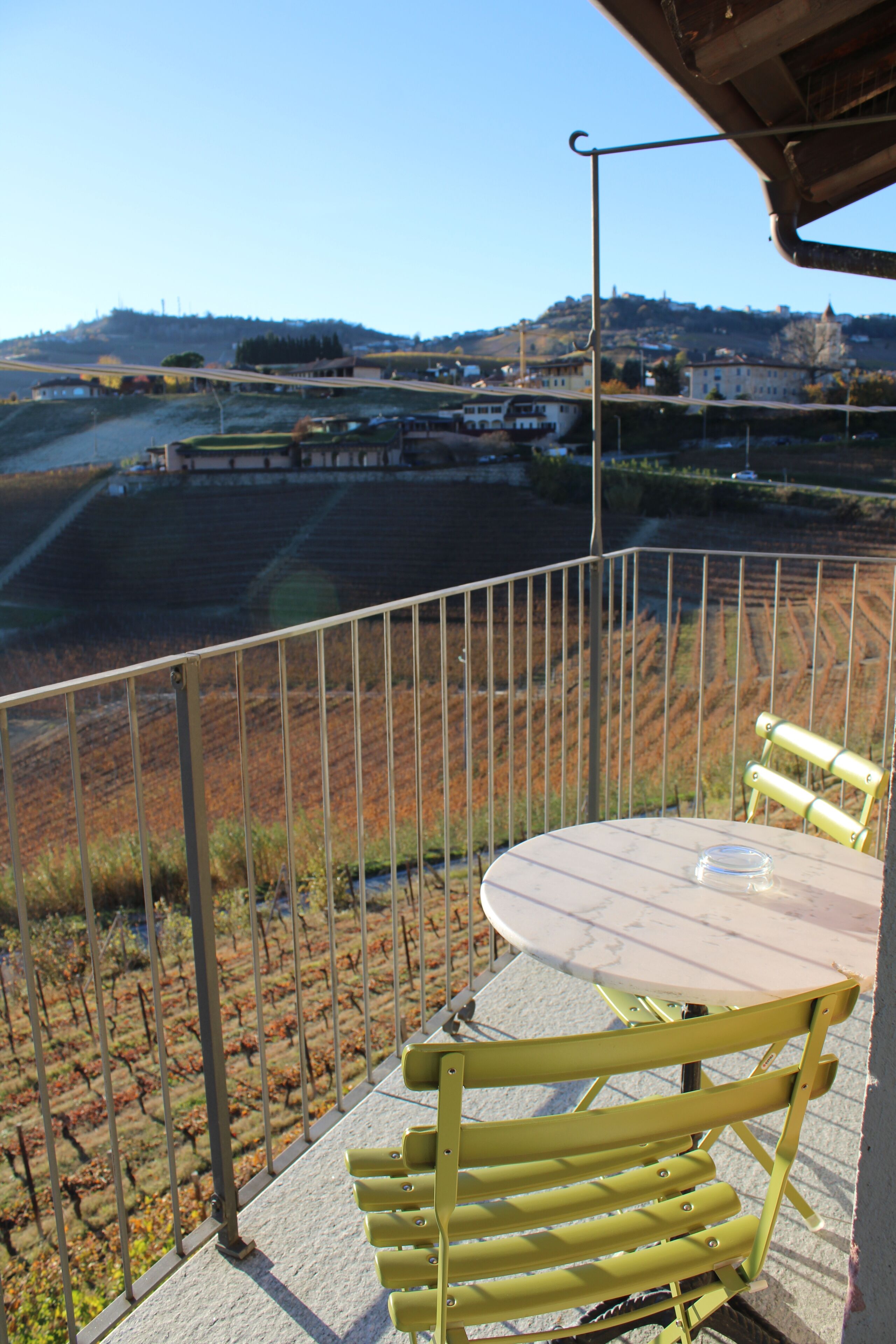 A balcony with a table and chairs, overlooking a vineyard and a bridge.