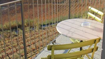 A balcony with a table and chairs, overlooking a vineyard and a bridge.