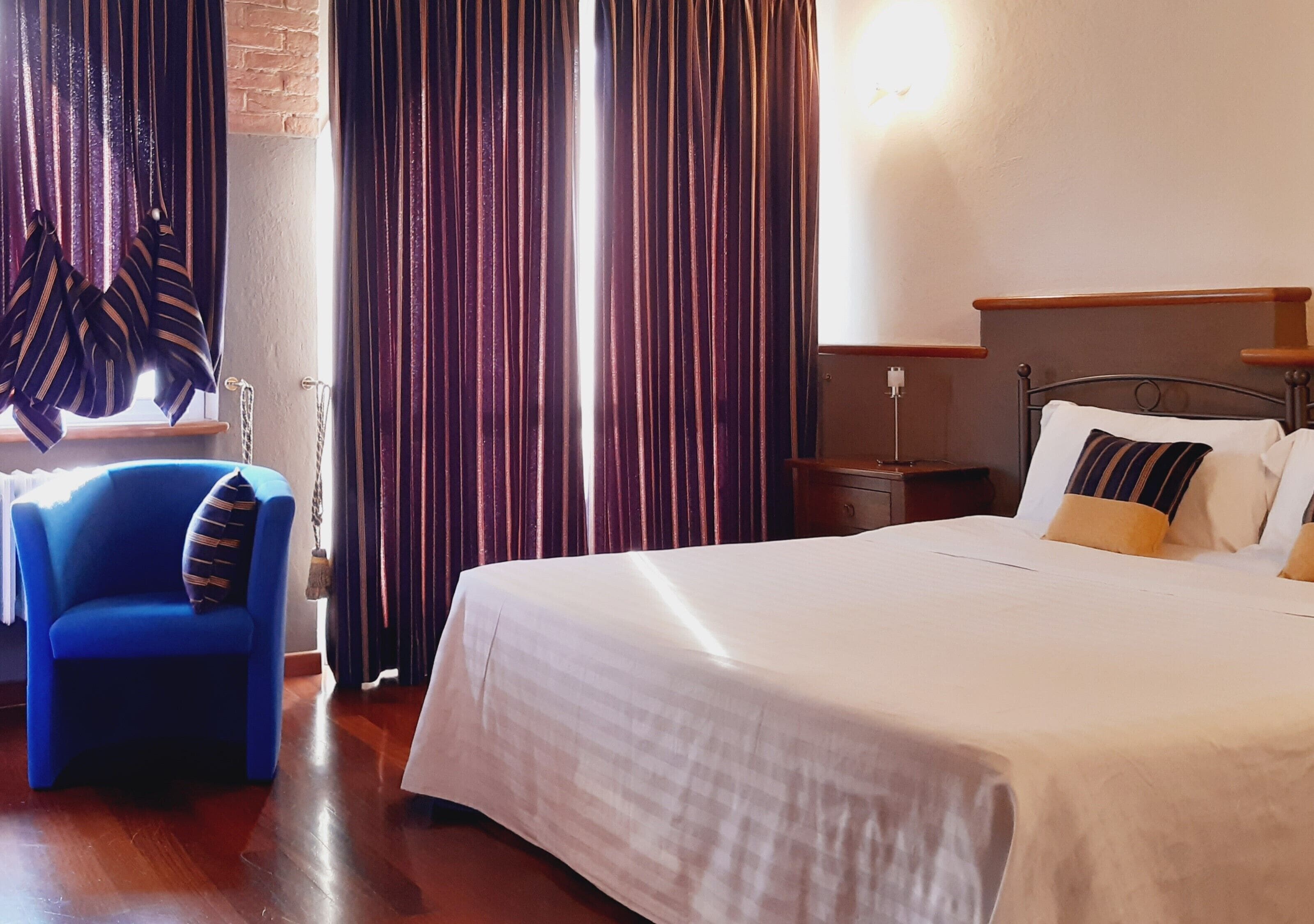 Ein Hotelzimmer mit Bett, Stuhl, Vorhängen und Nachttisch.