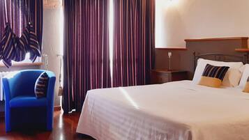 Ein Hotelzimmer mit Bett, Stuhl, Vorhängen und Nachttisch.