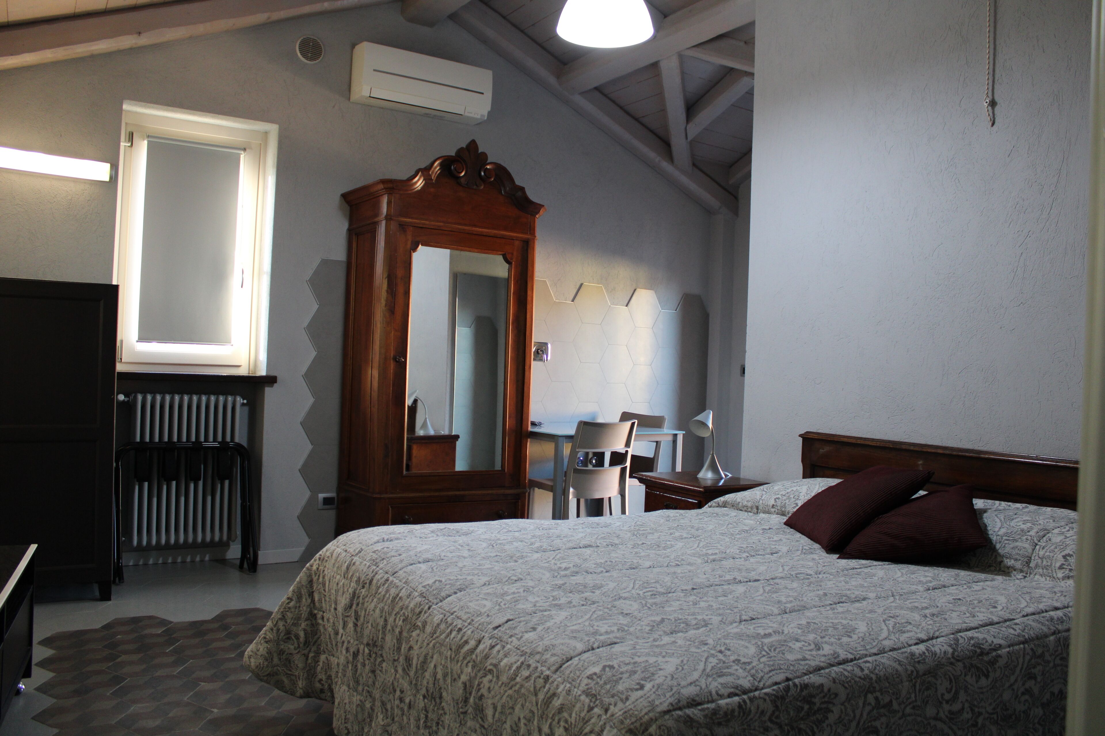 Un dormitorio con cama, un armario de madera, un escritorio con silla, un radiador y un espejo grande.