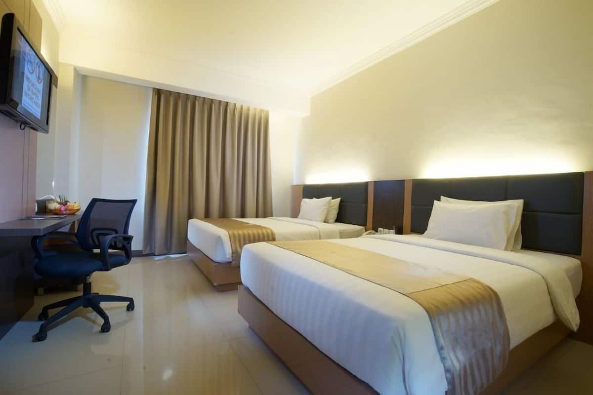 A hotel room with two beds, a desk, a chair, and a TV mounted on the wall.