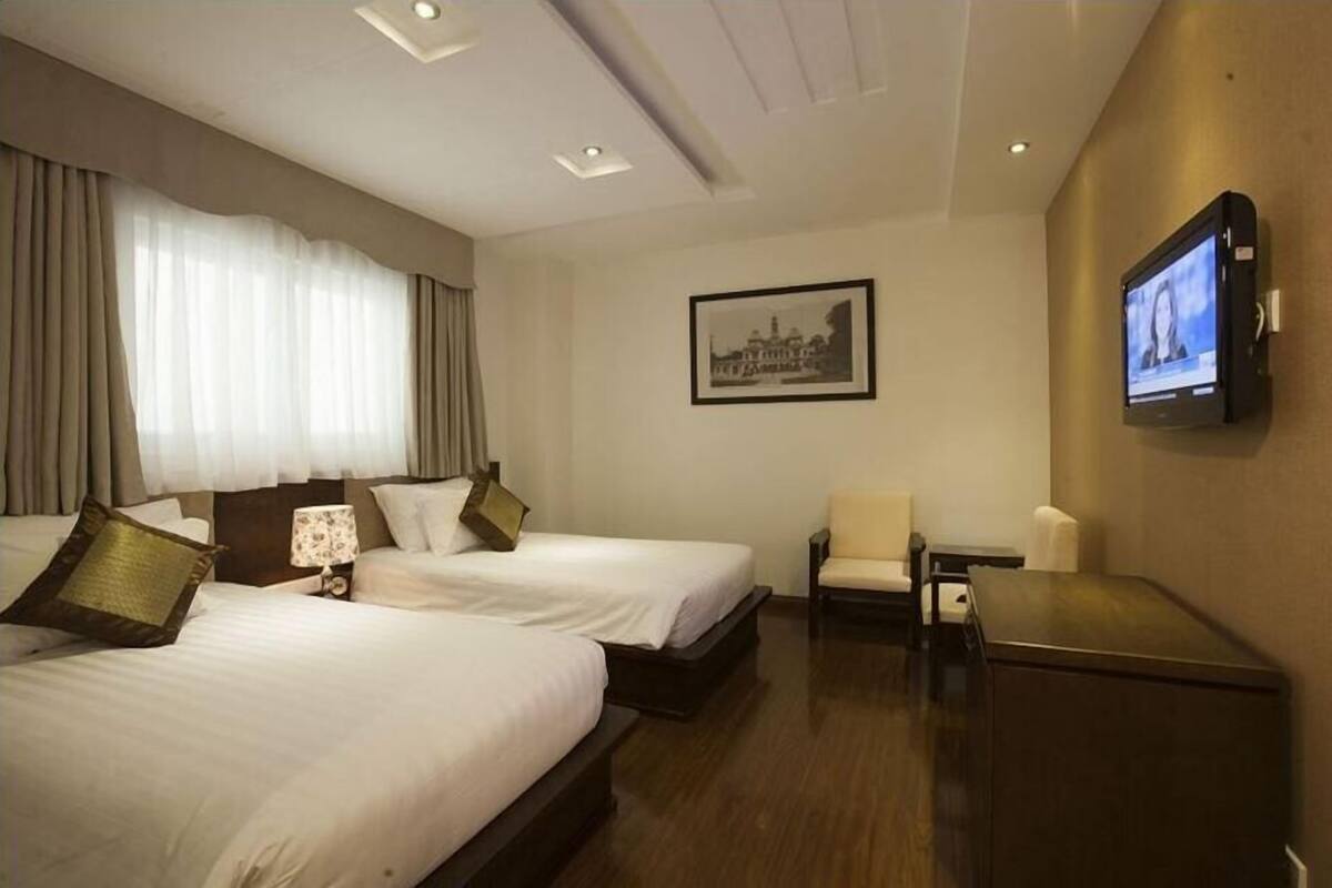 A hotel room with two beds, a television, a chair, and a desk.