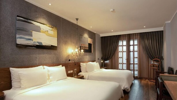 A hotel room with two beds, a large window with curtains, a chandelier, and a wall art piece. - Hanoi Discovery Hotel (Hanoi)