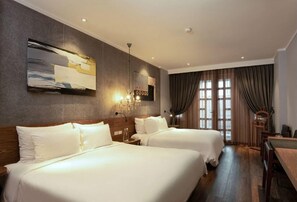 Habitación de hotel con dos camas, un ventanal con cortinas, un candelabro y una obra de arte en la pared.