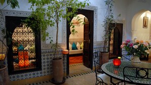 Un interior tradicional marroquí con paredes y suelo de azulejos, una mesa redonda con sillas y una planta en maceta.