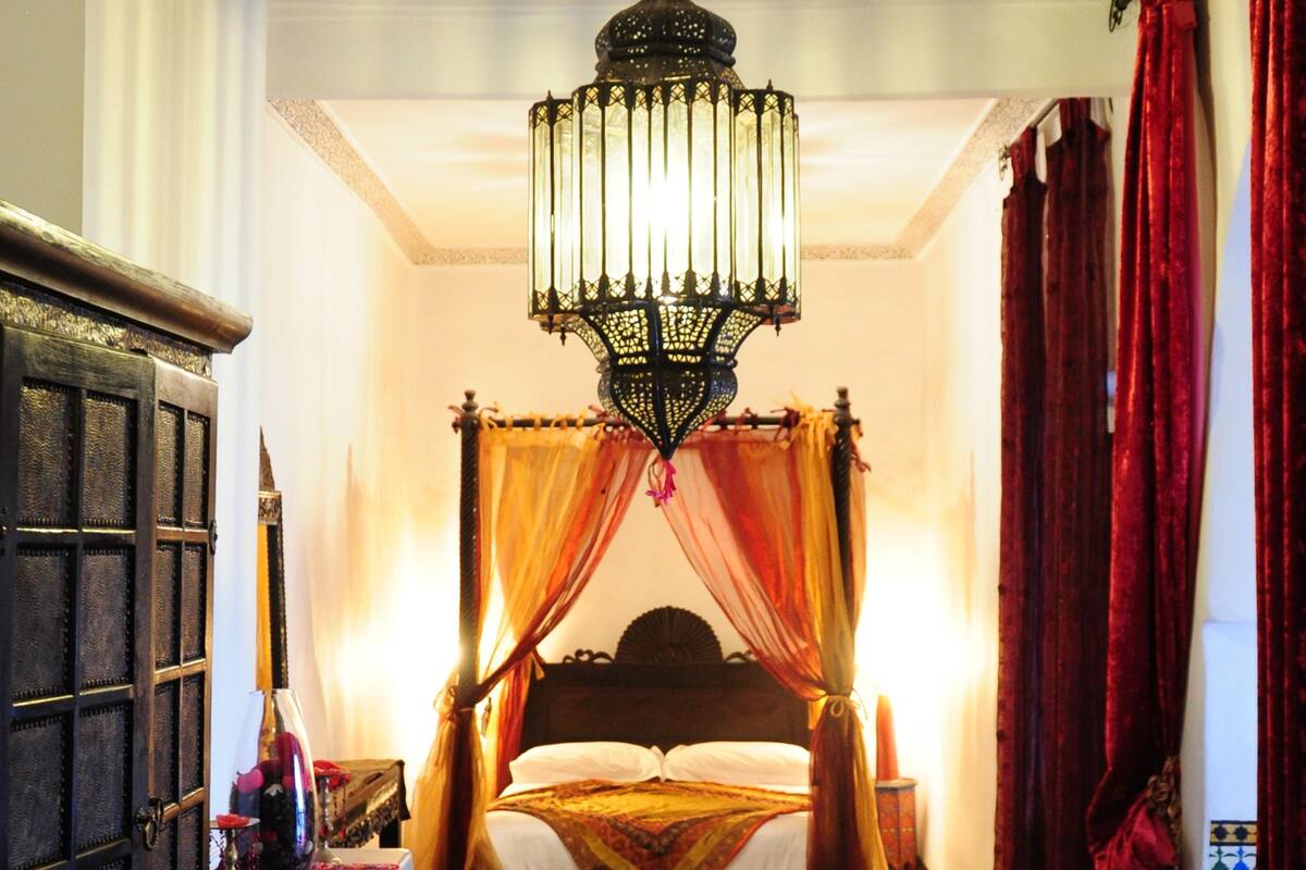 A traditional bedroom with a four-poster bed, ornate chandelier, and red drapes.