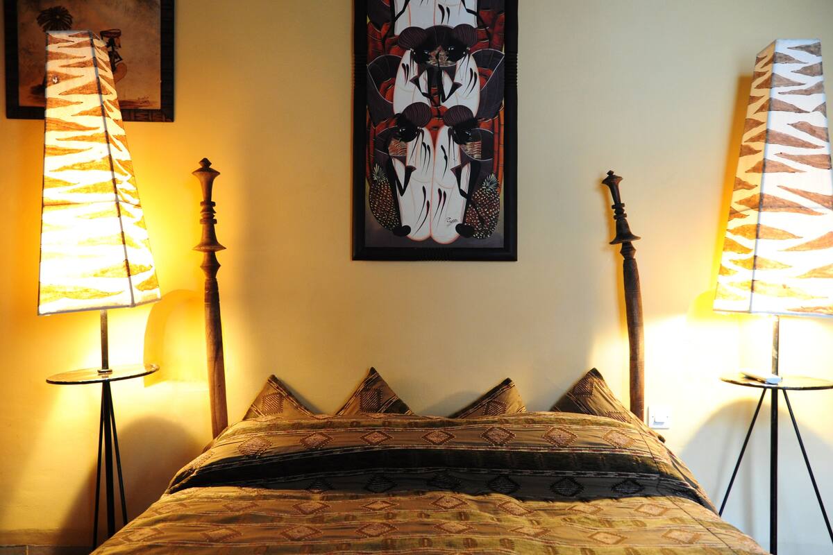 A bed with patterned bedding, two standing lamps, and a framed artwork on the wall.