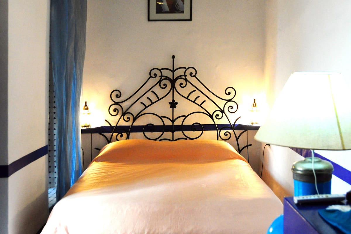 A bedroom with a bed, a nightstand, a lamp, a hanging light fixture, and a picture on the wall.