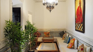 Un interior tradicional marroquí con un muro estampado, un banco de madera con cojines y una lámpara de araña colgante.