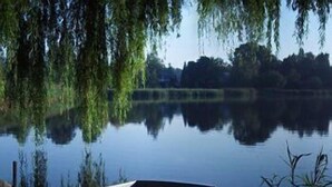 Een houten roeiboot, vastgemaakt aan een steiger aan een rustig meer, met bomen op de achtergrond.