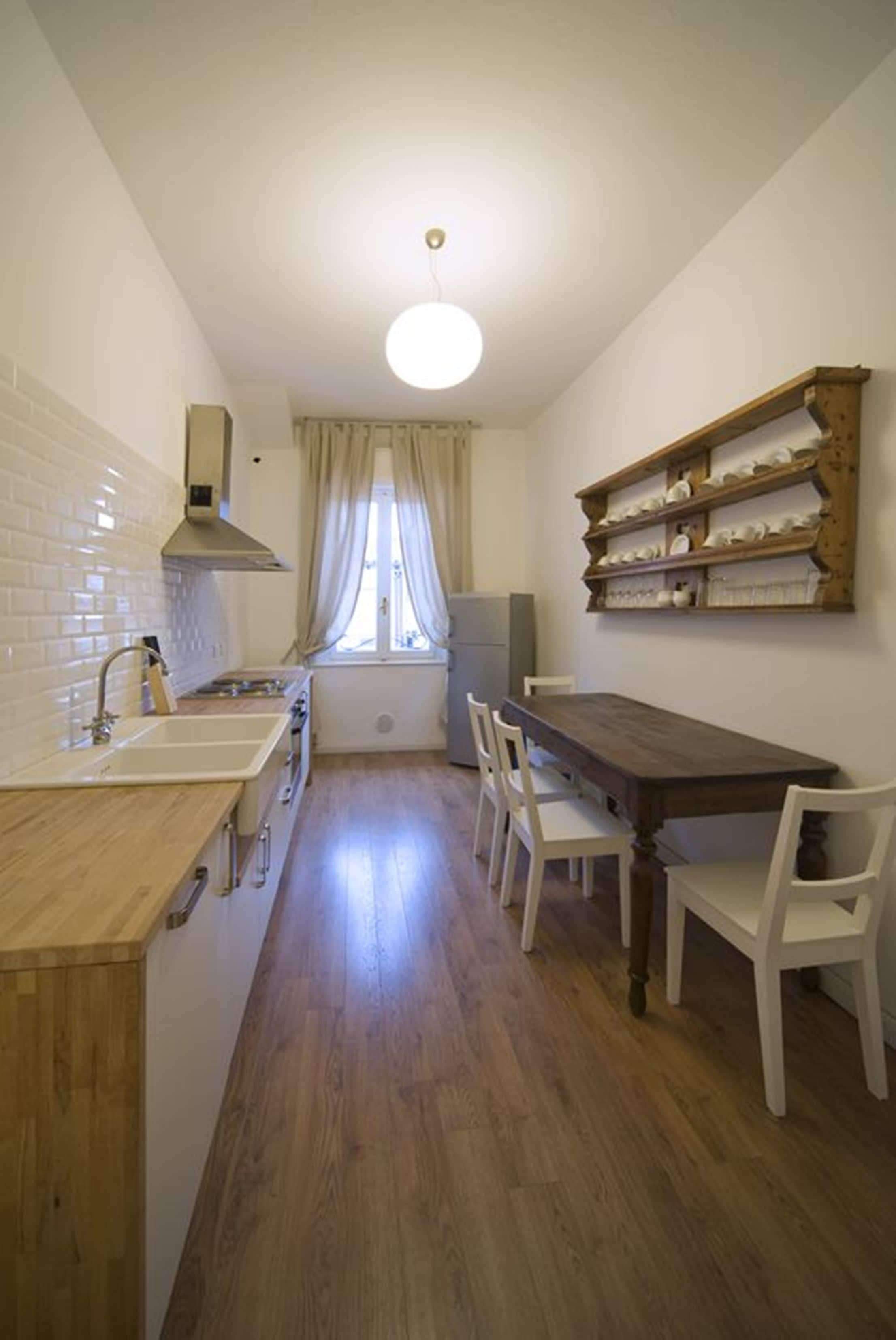 A kitchen with a wooden countertop, white chairs, a wooden dining table, and a window with curtains.