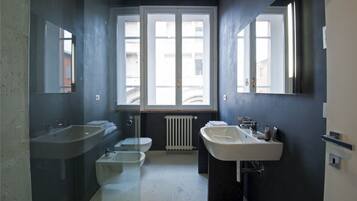Een moderne badkamer met twee wastafels, een toilet en een raam voor natuurlijk licht.