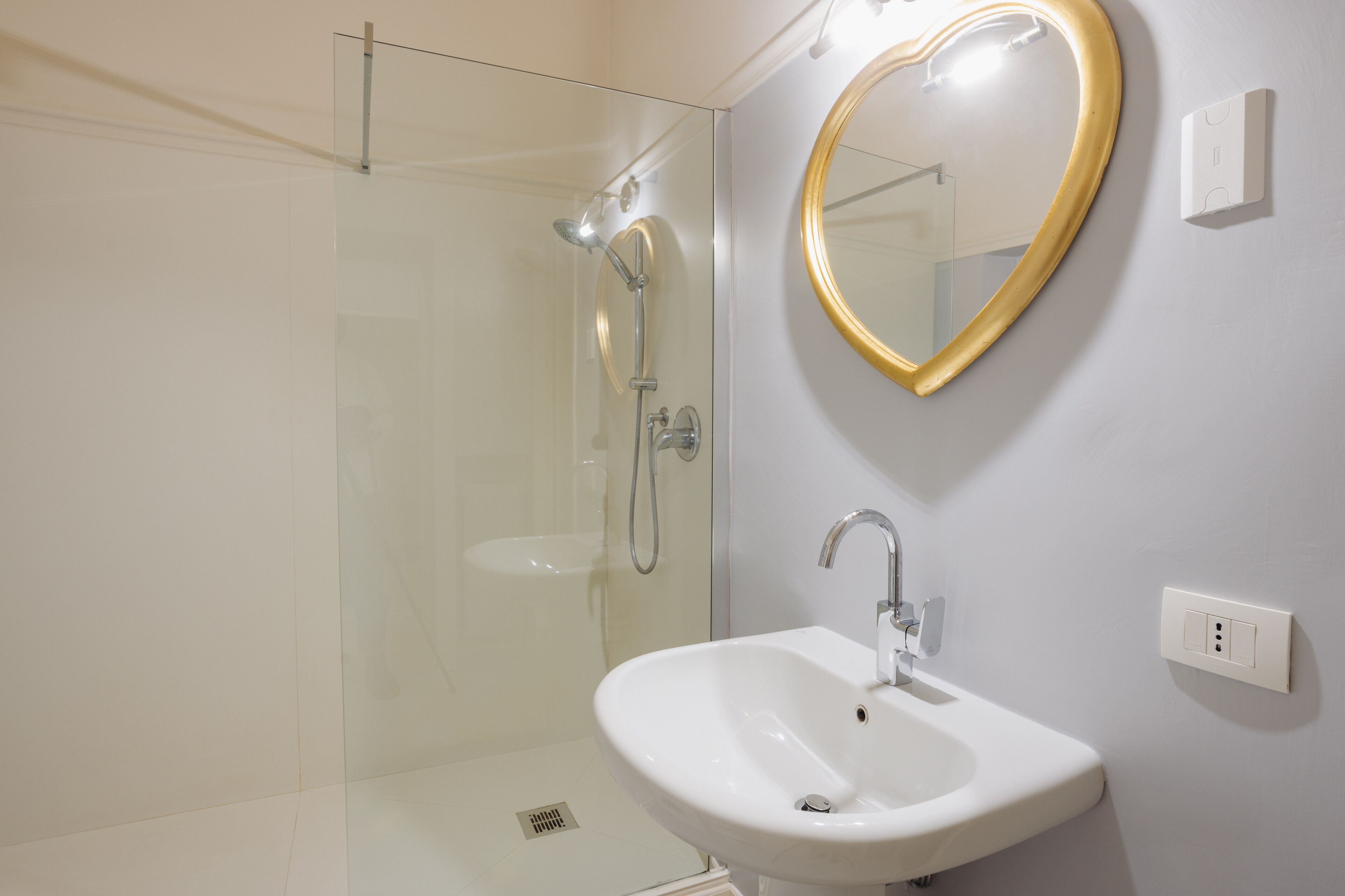 Une salle de bain moderne avec une douche en verre, un lavabo blanc et un miroir en forme de cœur.