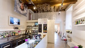 Zona de bar moderna con una barra larga, estantes con botellas y una pantalla de televisión.