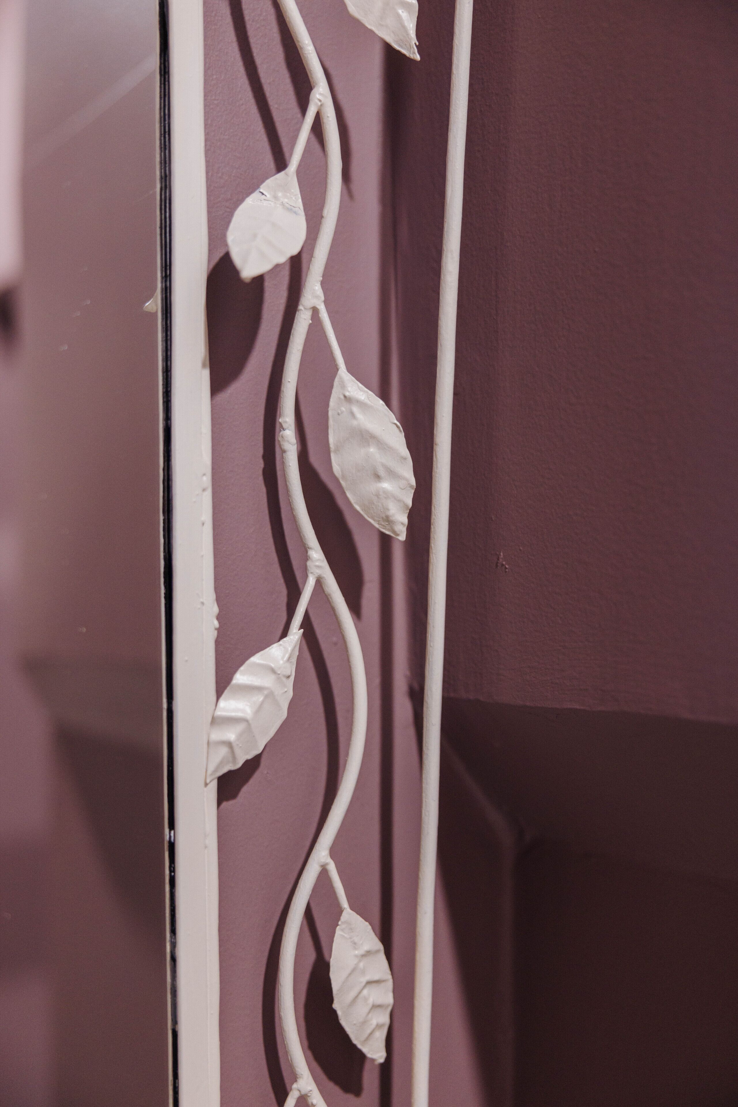 Eine weiße, dekorative Metalldranke mit Blättern vor einer violetten Wand.