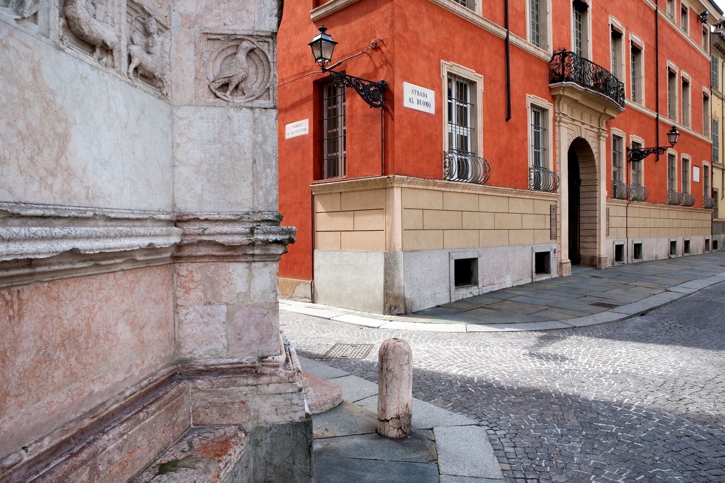 A cobblestone street with a red building featuring a sign that reads "Strada Al Duomo."
