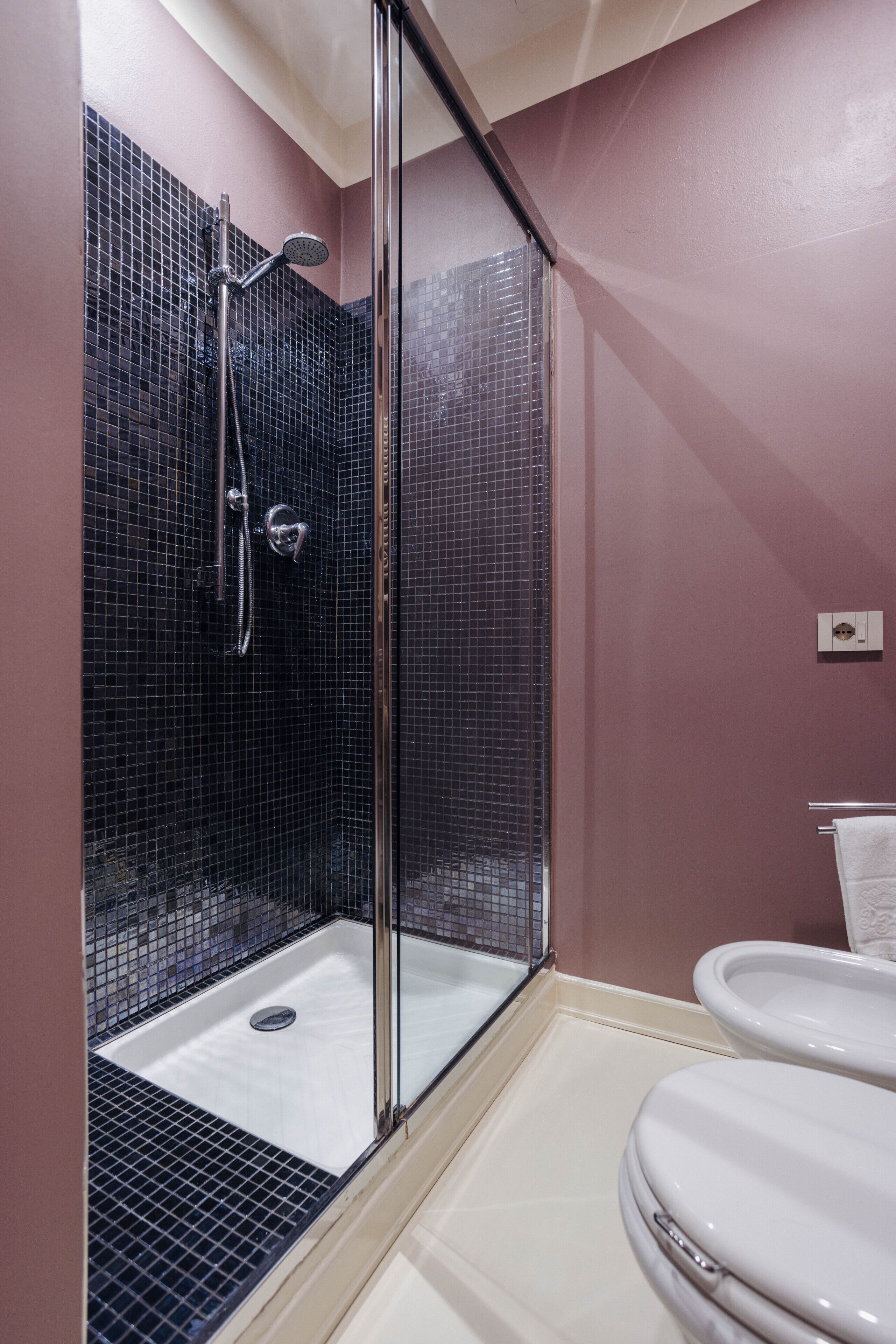 A shower with a glass door, a toilet, and a tiled floor.