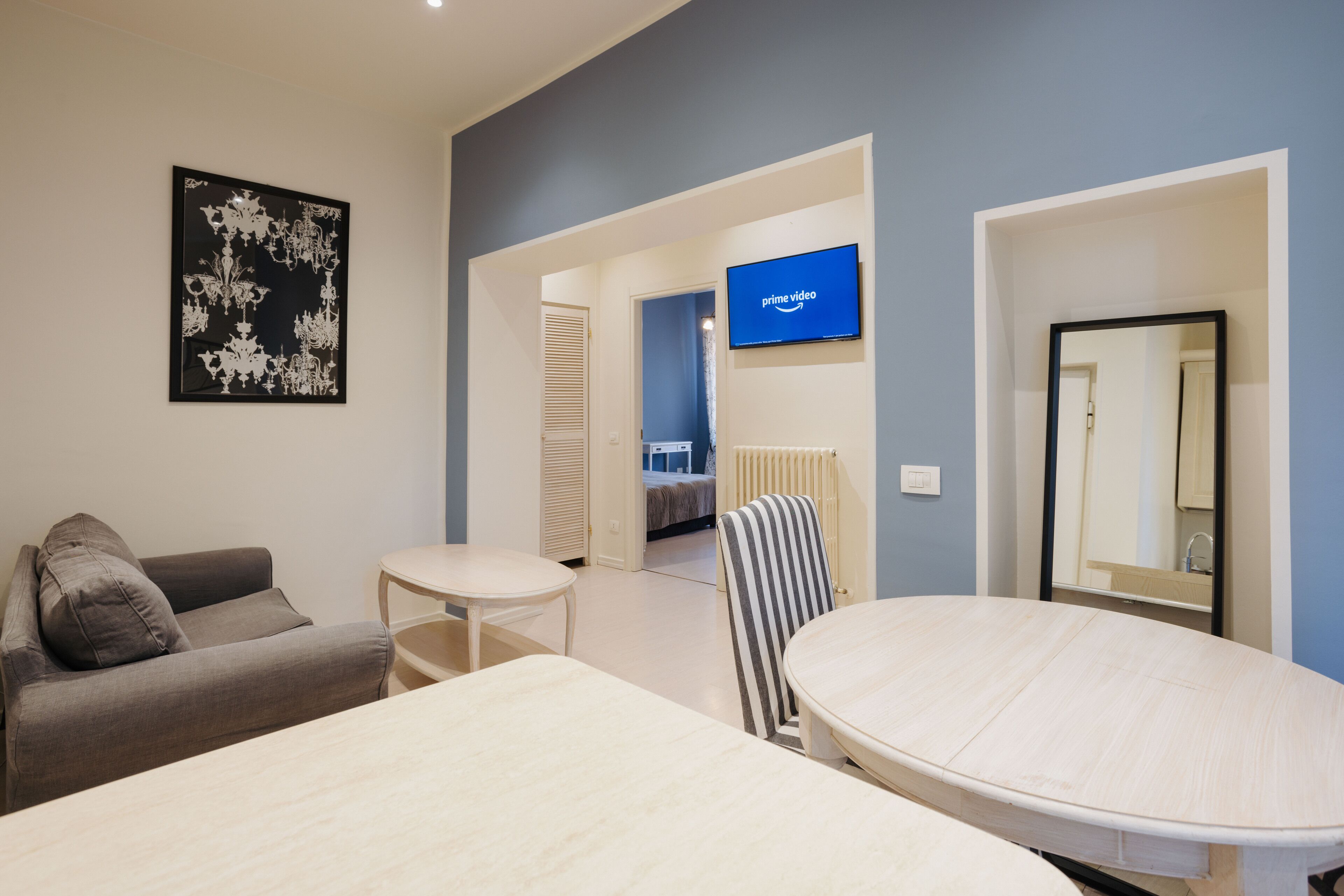 A modern room with a sofa, a round table, a striped chair, a flat-screen TV, and a large mirror.