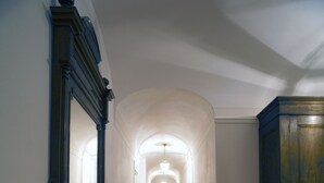 Un pasillo estrecho con piso de madera, paredes blancas y un espejo grande a la izquierda.