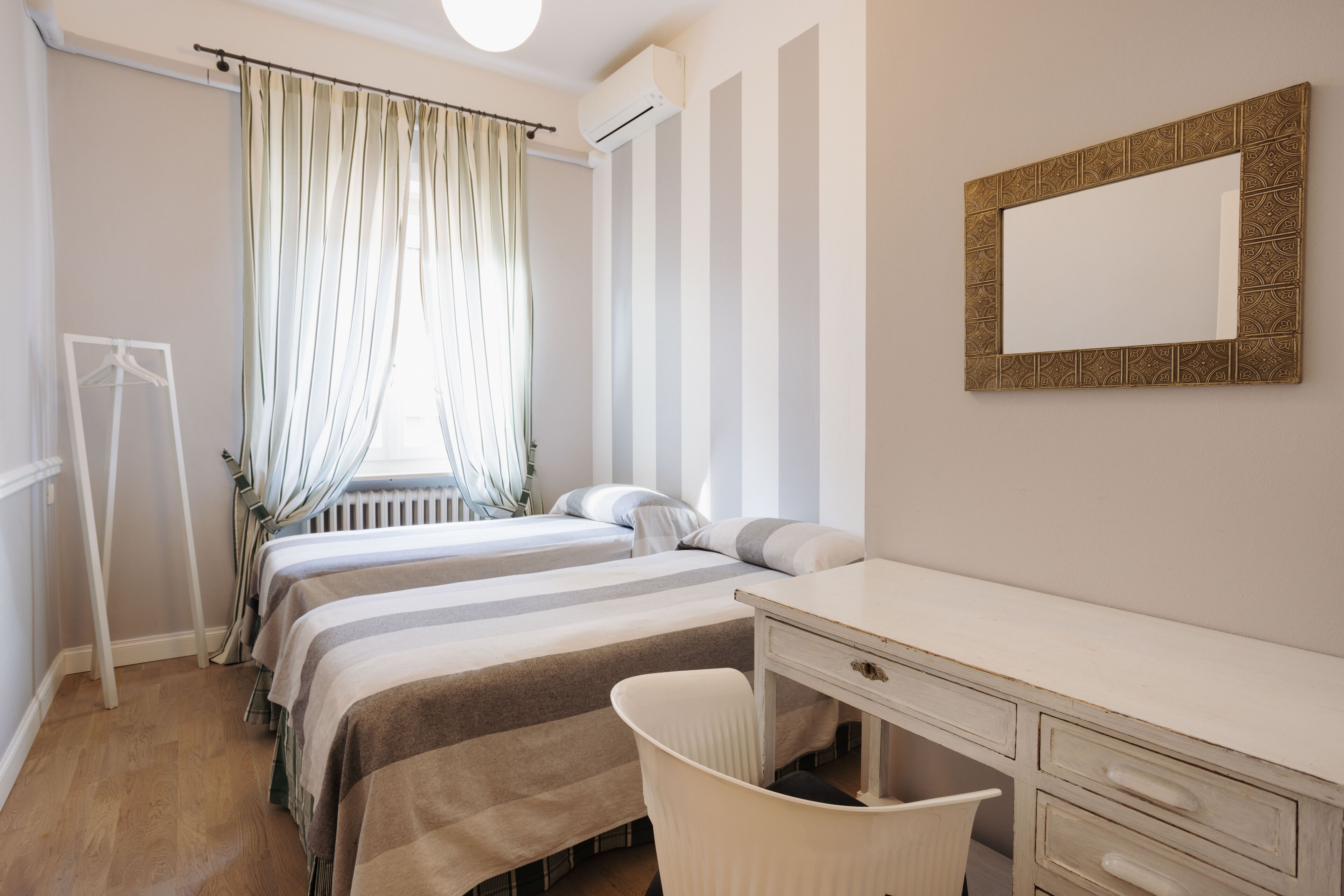 Una habitación de hotel con dos camas, un escritorio, una silla, un radiador y un espejo.