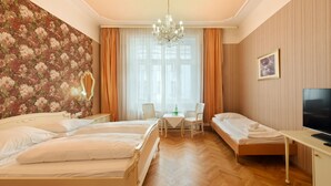Quarto de hotel com duas camas, um candelabro, uma televisão e papel de parede floral.