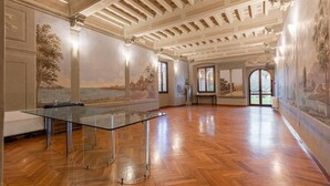 Een ruime kamer met een tafel met glazen blad, houten vloer en klassieke balkenplafond.