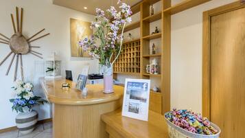 Un espace d’accueil avec un comptoir en bois, un vase rempli de fleurs, un panneau indiquant la présence de la page Facebook de l’entreprise, et un bol de bonbons.