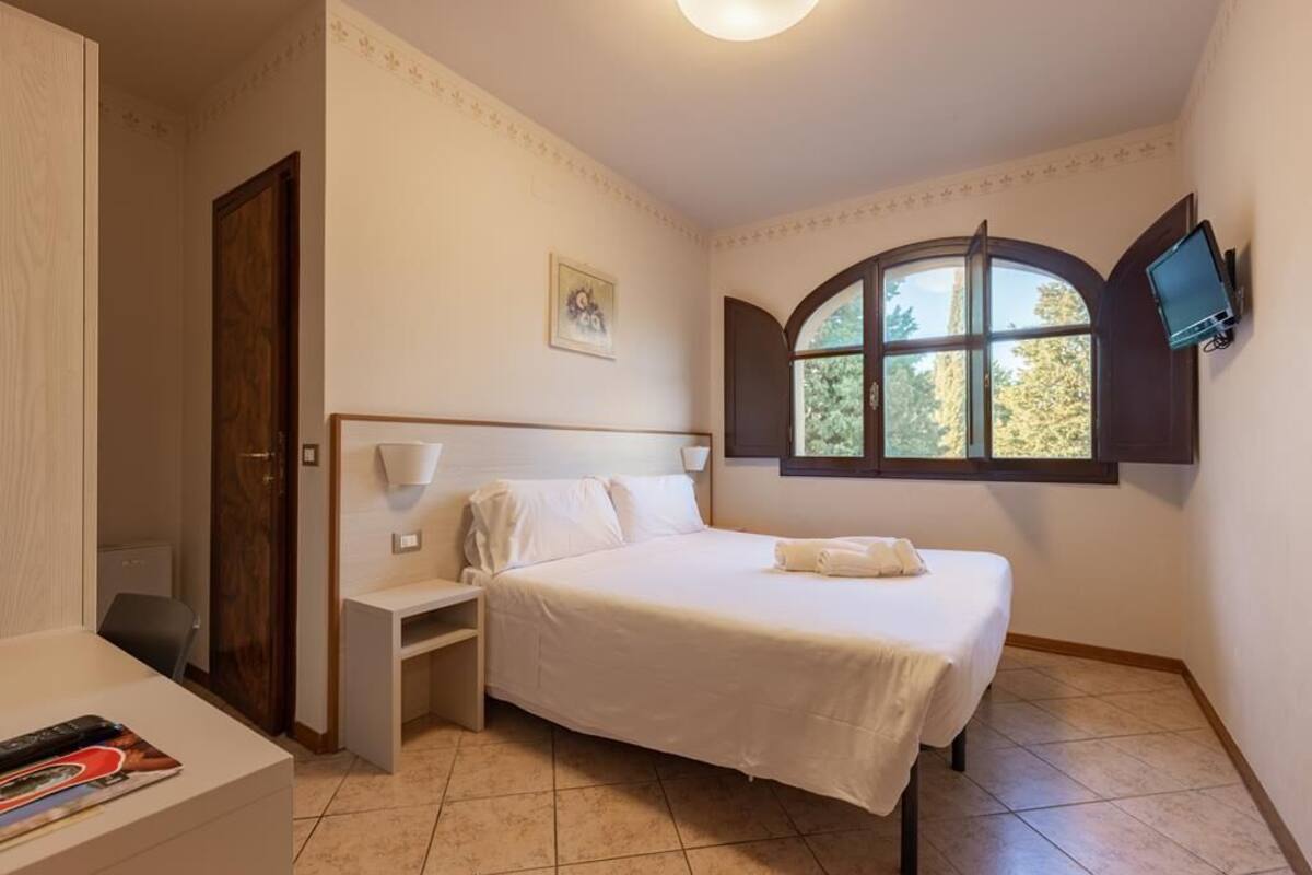 Une chambre à coucher comprenant un lit, une table de chevet, un bureau, une chaise, une fenêtre avec vue et un téléviseur fixé au mur.