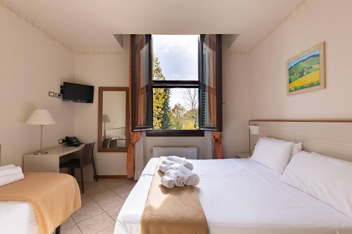 Une chambre d’hôtel avec un lit, un bureau, une chaise, une télévision et une fenêtre avec des rideaux.