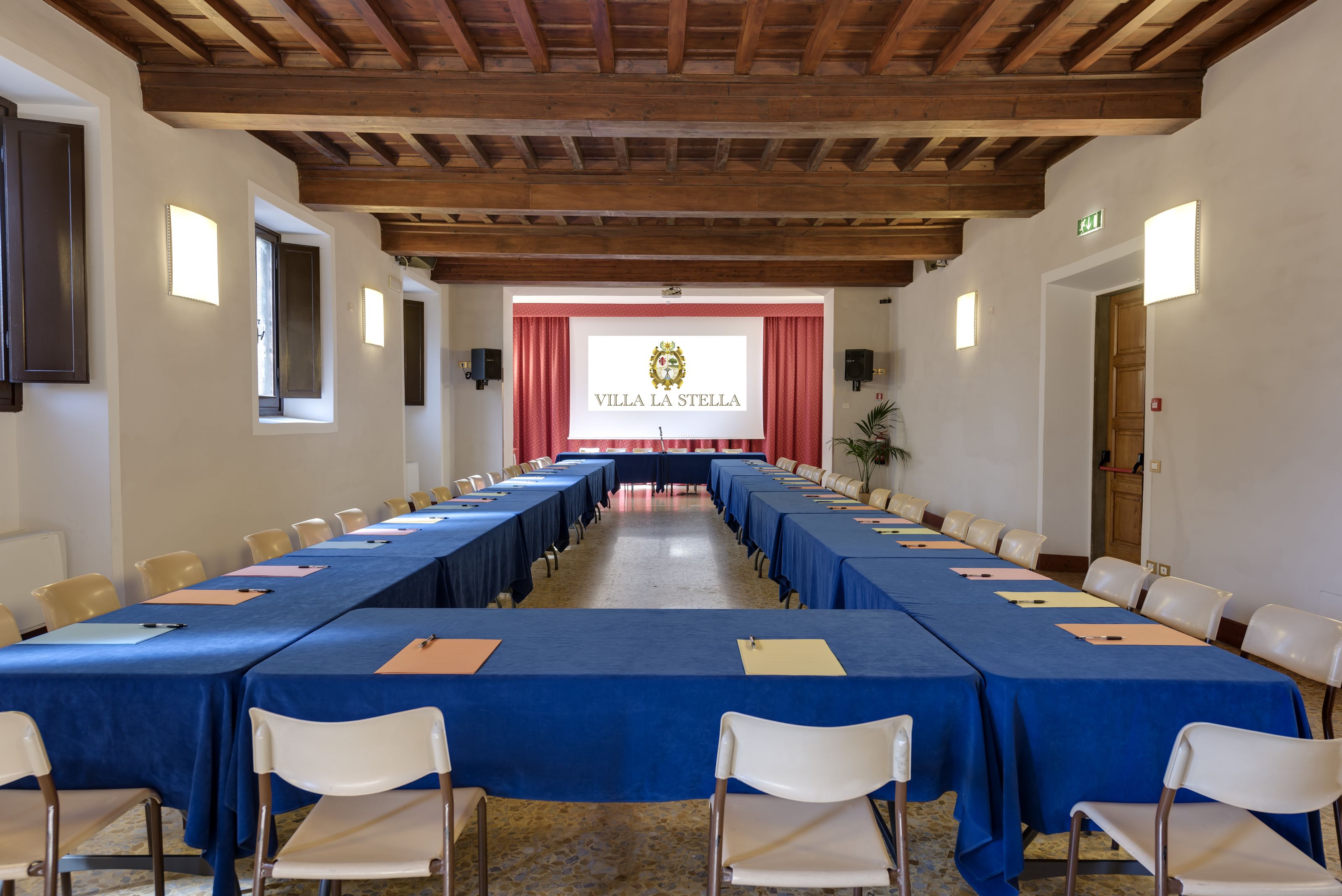 A conference room with a long table, white chairs, and a red curtain backdrop with the text "VILLA LA STELLA".