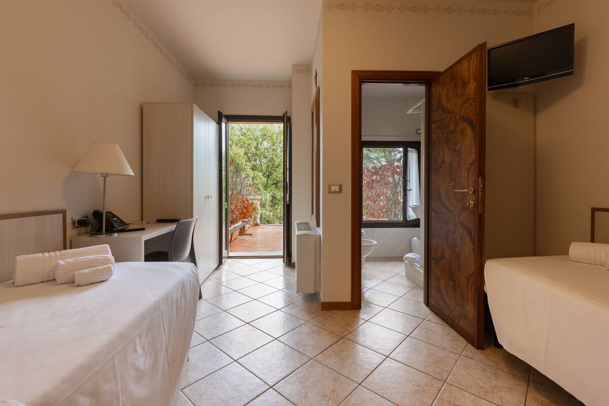 Une chambre d’hôtel avec deux lits, un bureau avec une lampe, un téléviseur fixé au mur et une vue sur l’extérieur.