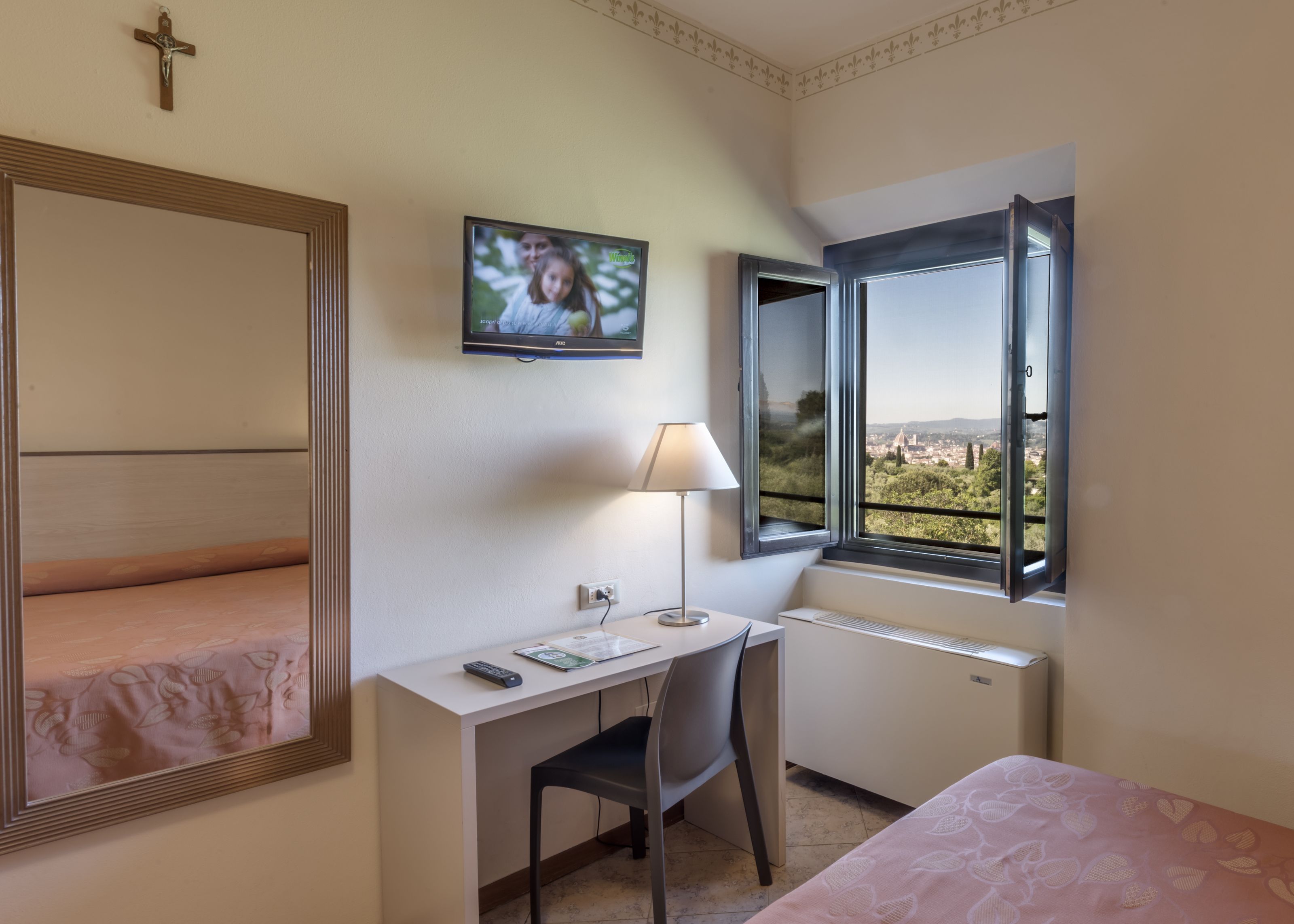 Ein Hotelzimmer mit Bett, Schreibtisch mit Stuhl, Wandfernseher und einem Fenster mit Blick auf eine Skyline.