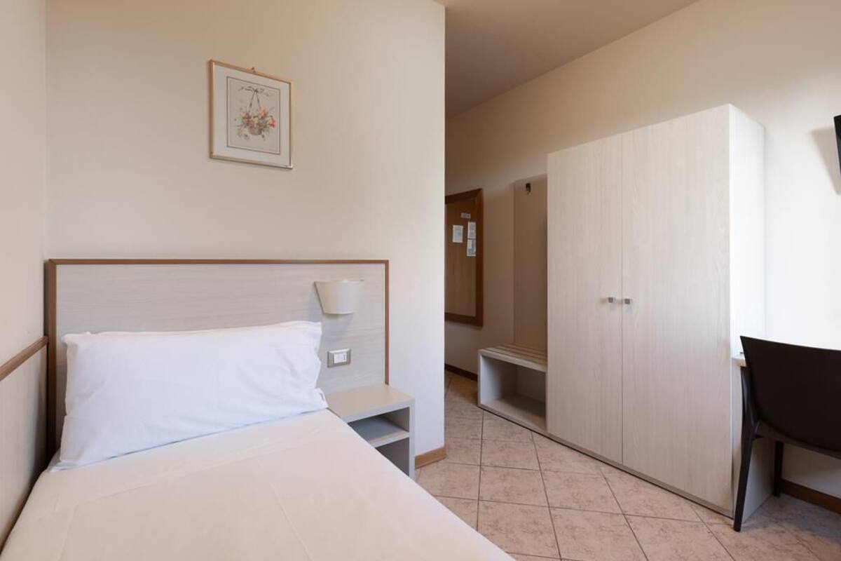 Une chambre d’hôtel comprenant un lit, une table de chevet, une lampe, une armoire et une chaise.