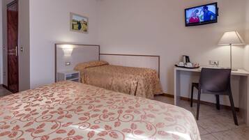 A hotel room with a bed, a desk, a chair, a television, and a painting on the wall.