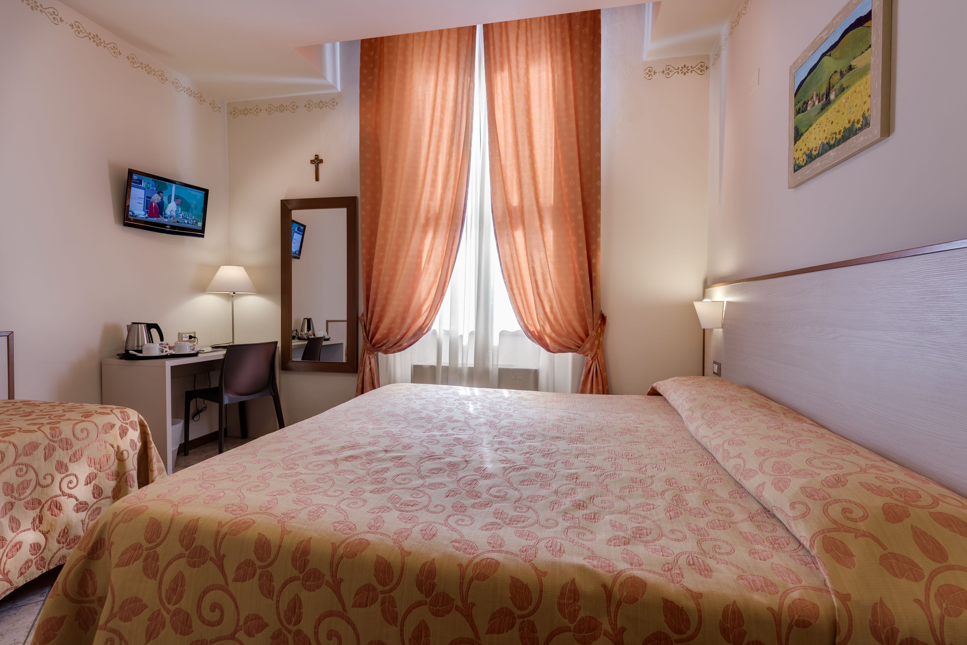 Een hotelkamer met twee bedden, een bureau met stoel, een televisie en een schilderij aan de muur.