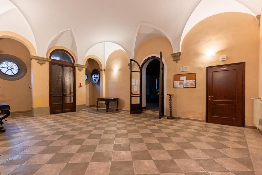 A spacious hallway with checkered flooring, arched ceilings, and multiple doors leading to different rooms.