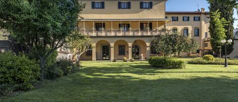 A two-story building with a balcony, arched doorways, and a well-maintained lawn.