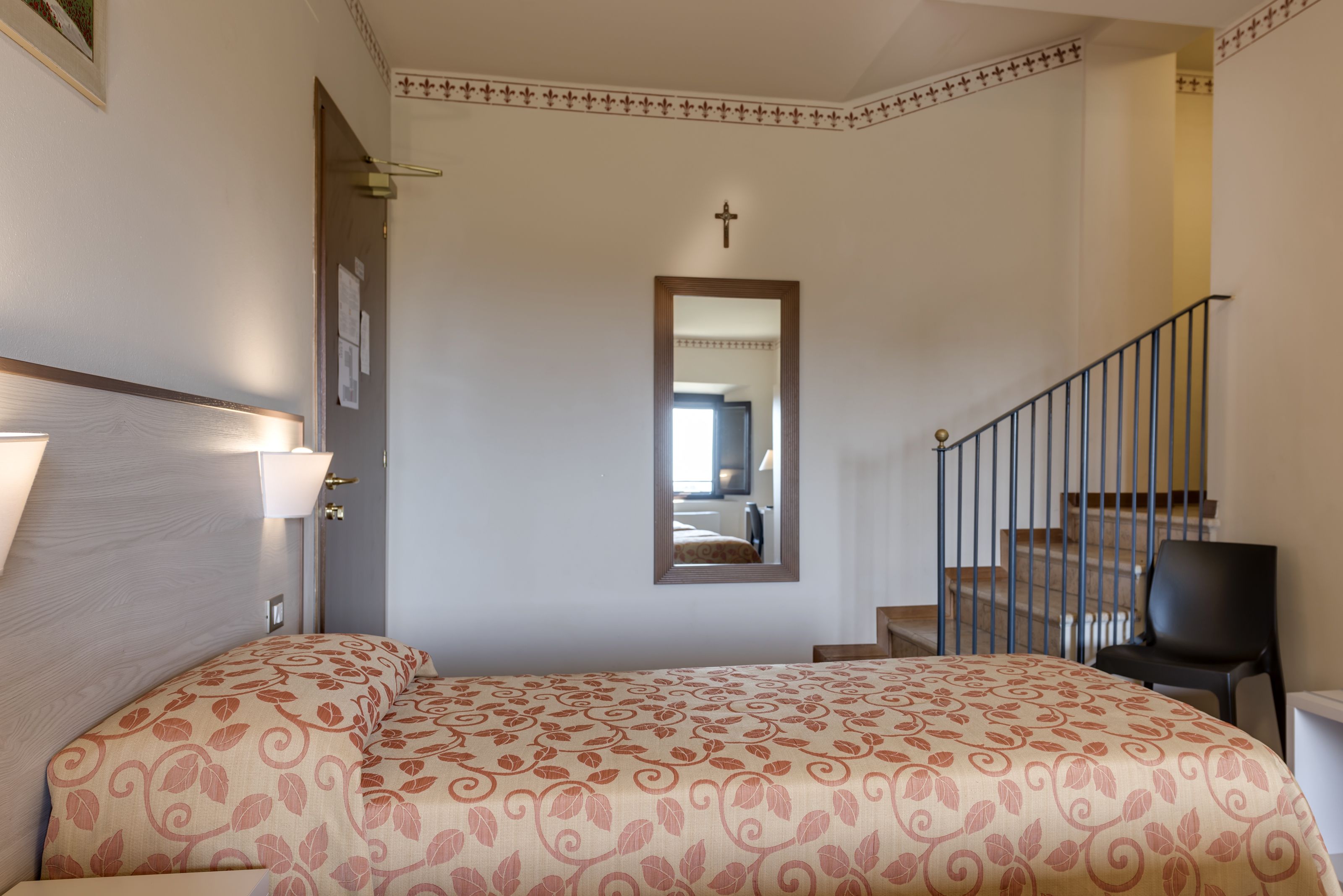 A bedroom with a bed, a mirror, a staircase, and a cross on the wall.