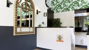 A reception area with a large arched mirror, a clock, and a wall with a tropical leaf pattern. - Quentin Canal House Hotel (Amsterdam)