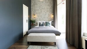 A bedroom with a large bed, a bench, a patterned wallpaper, and a hanging light fixture. - Quentin Canal House Hotel (Amsterdam)
