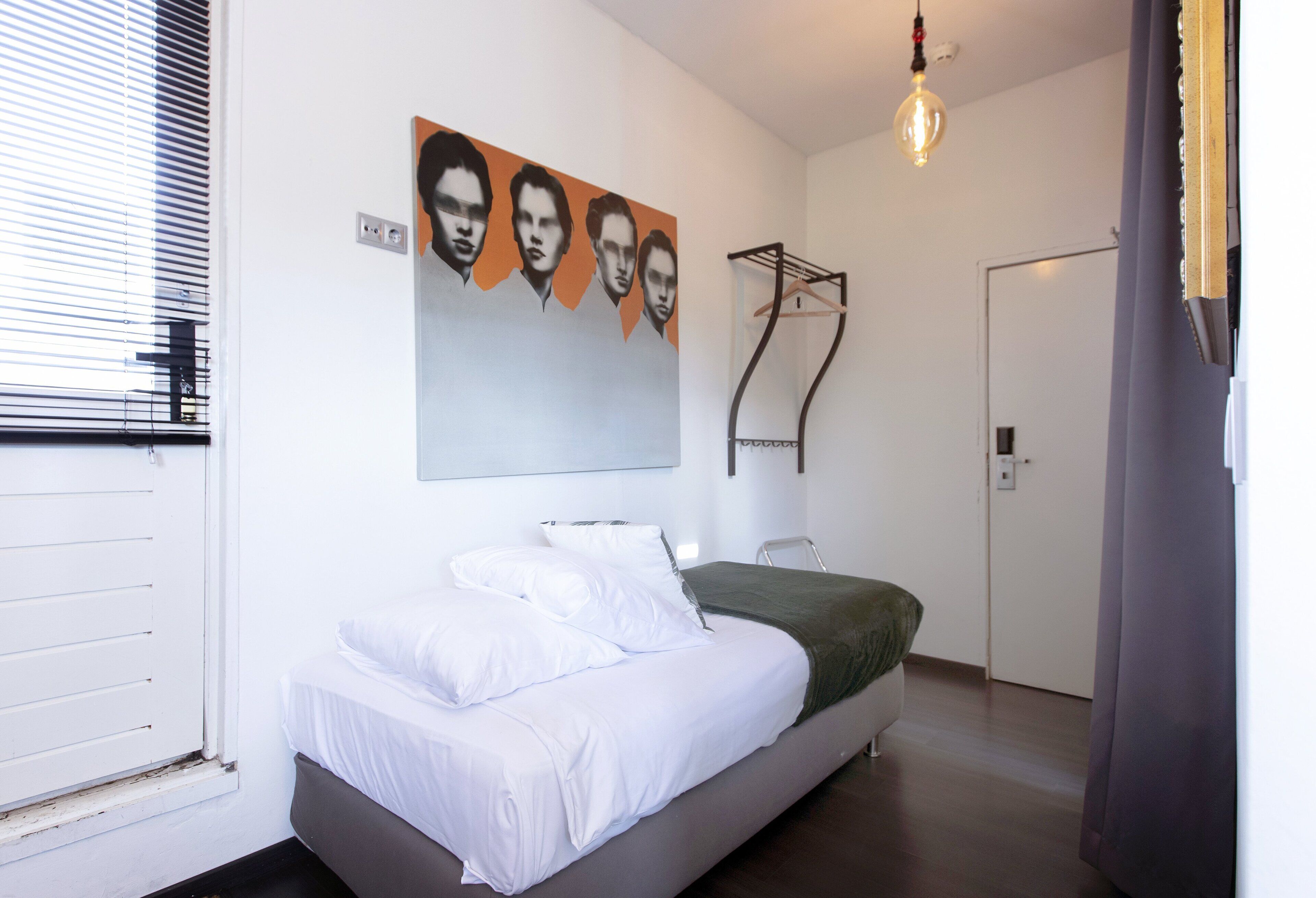 Un dormitorio moderno con cama, ropa de cama blanca, una obra de arte en la pared, una lámpara colgante y una puerta.