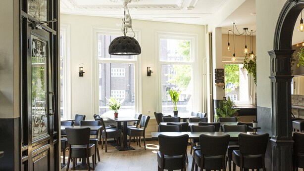 A spacious dining area with multiple tables and chairs, large windows allowing natural light, and decorative ceiling elements. - Quentin Canal House Hotel (Amsterdam)