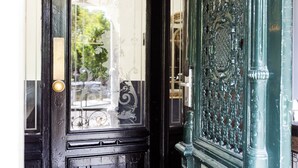 A black door with a brass handle and glass panel, featuring intricate metalwork and a view of greenery outside. - Quentin Canal House Hotel (Amsterdam)