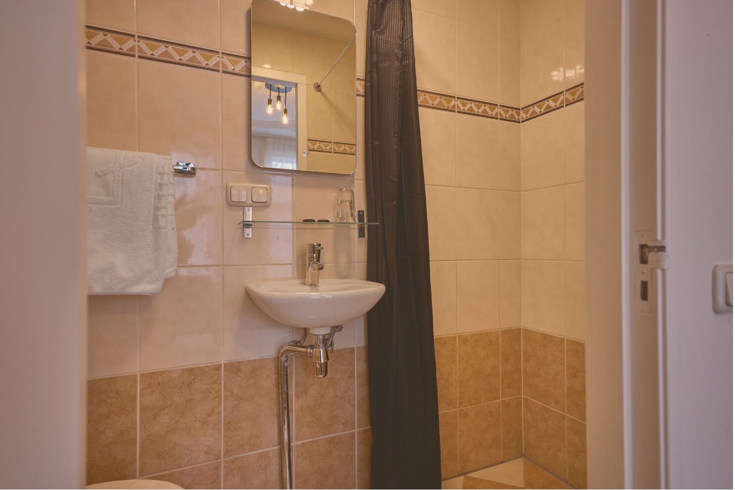 Un baño con lavamanos blanco, una toalla, un espejo y cortina de ducha.