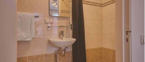 Un baño con lavamanos blanco, una toalla, un espejo y cortina de ducha.
