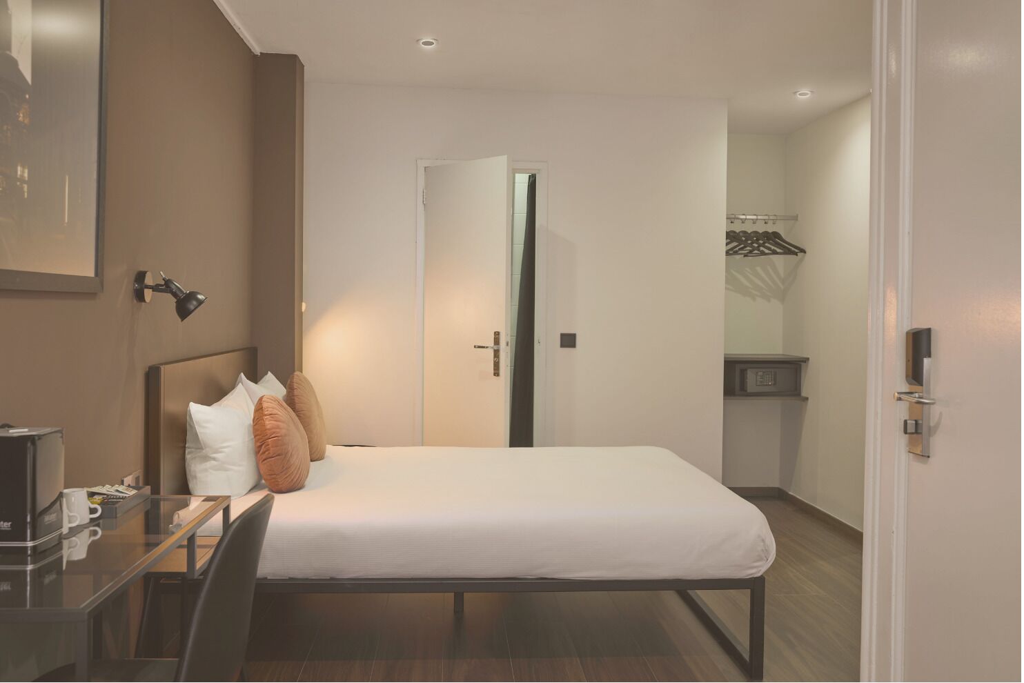A hotel room with a bed, bedside table, lamp, and a door leading to a bathroom.