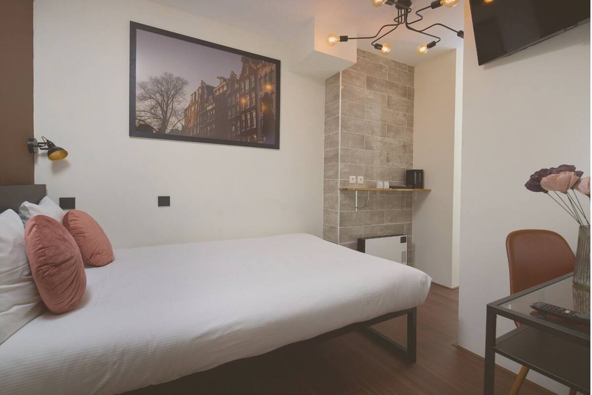 A hotel room with a bed, a desk, a chair, a TV, and a picture on the wall.