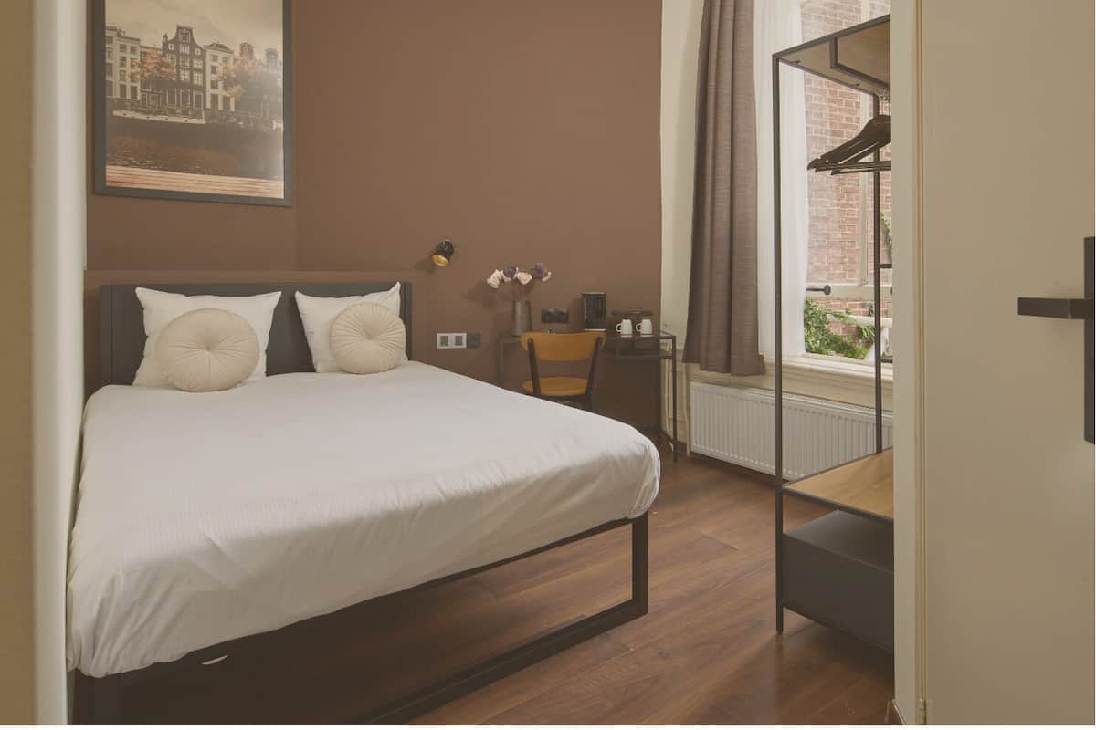 A bedroom with a bed, a nightstand, a chair, a window with curtains, and a framed picture on the wall.