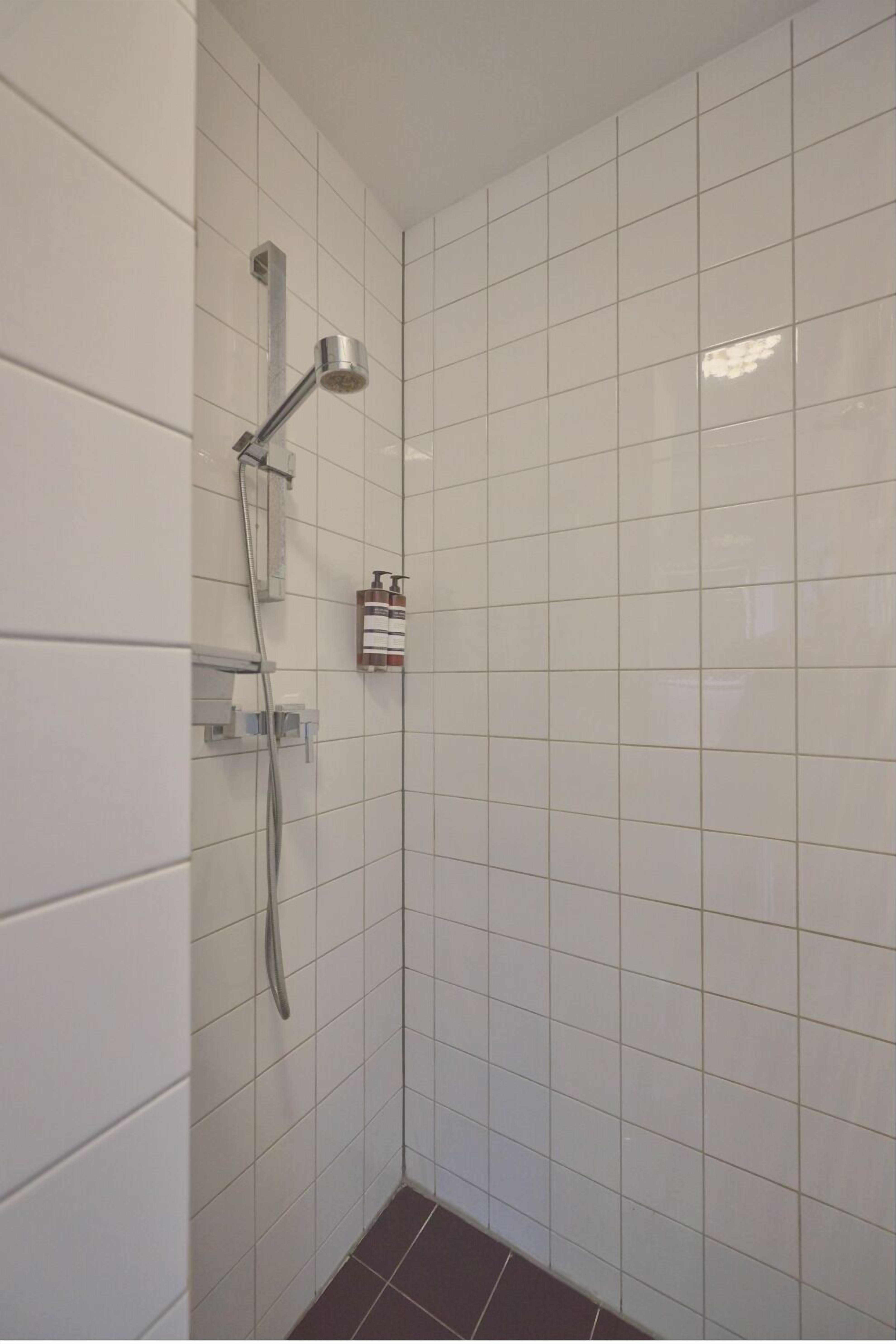 A small, tiled shower area with a handheld showerhead and a wall-mounted faucet.